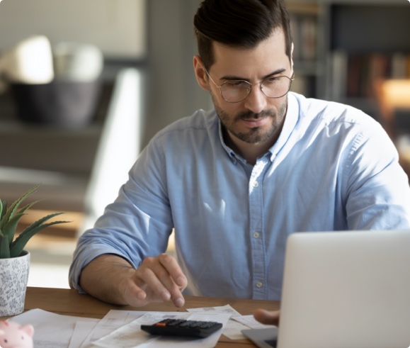 Focused young Caucasian man look at laptop screen calculate expenses expenditures pay bills taxes online. Millennial male busy managing household family budget, take care of financial paperwork.